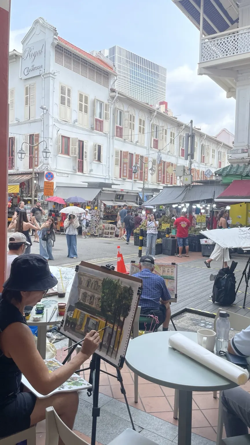 Eine Straßenmalerin arbeitet in Chinatown in Singapur vor historischen Häuserzeilen und Marktständen.