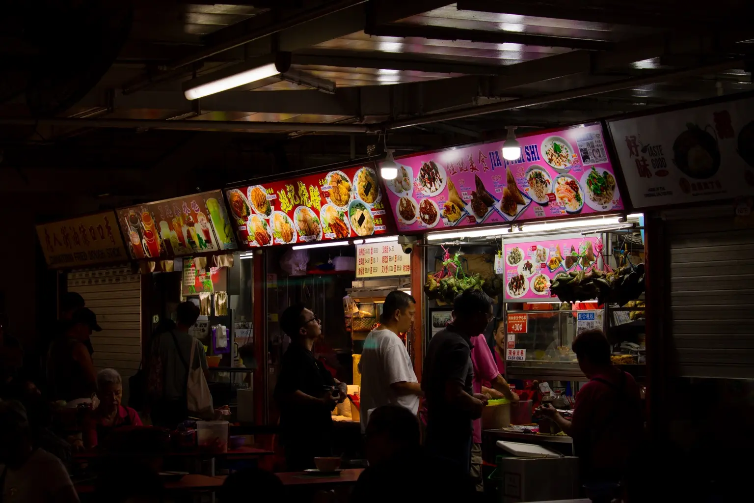 Beleuchtete Essensstände und Gäste in einem Hawker Centre in Singapur.