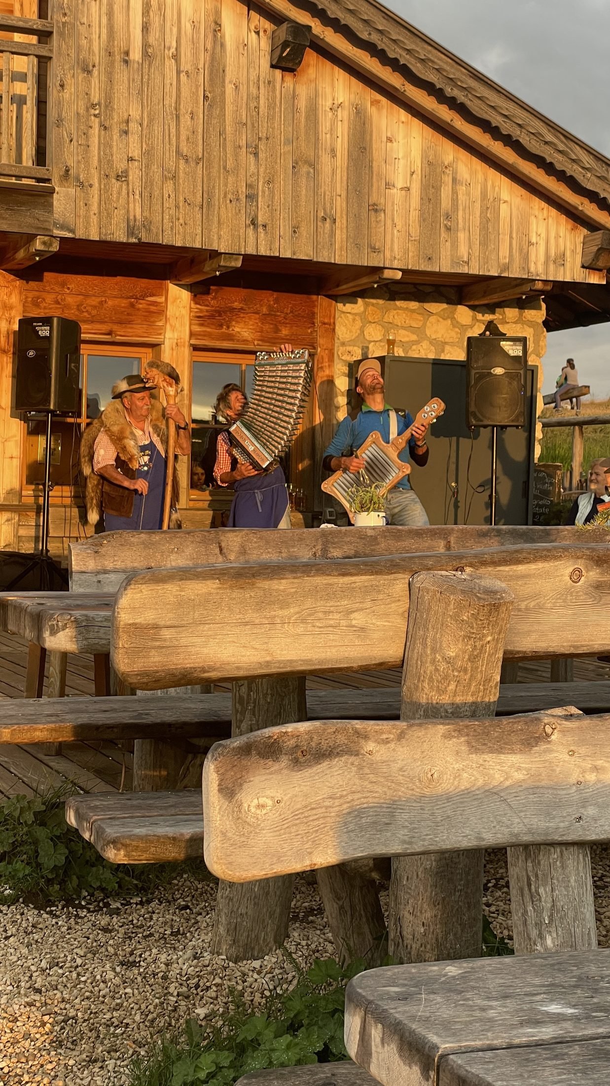 Drei Musiker spielen bei goldenem Abendlicht vor einer Berghütte in den Dolomiten