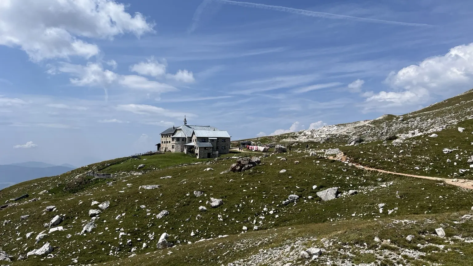 Das Schlernhaus steht auf einem grünen Hochplateau zwischen hellen Felsen und weitem Himmel.