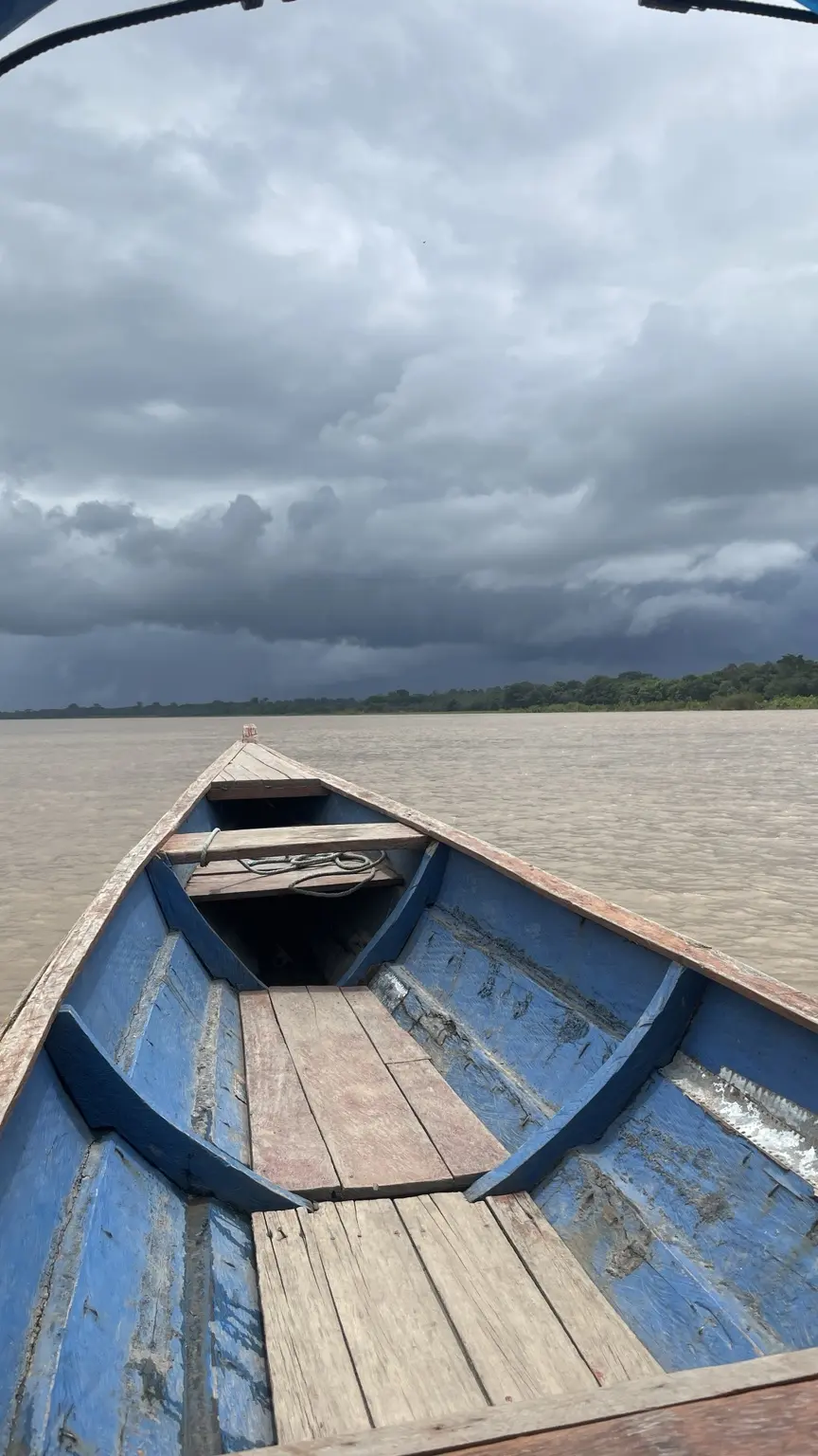 Blick aus einem Holzboot auf den Amazonas unter dunklen Wolken