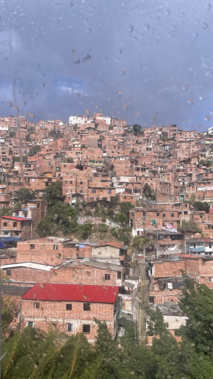 Blick auf dicht bebaute Häuser an einem Hang in Medellín durch eine regennasse Scheibe