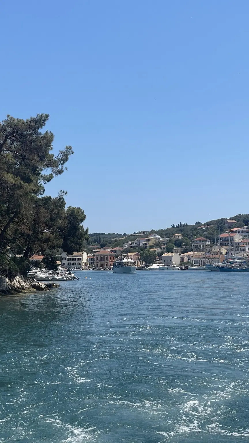 Blick vom Boot auf einen Hafen mit Häusern und Segelbooten auf Paxos