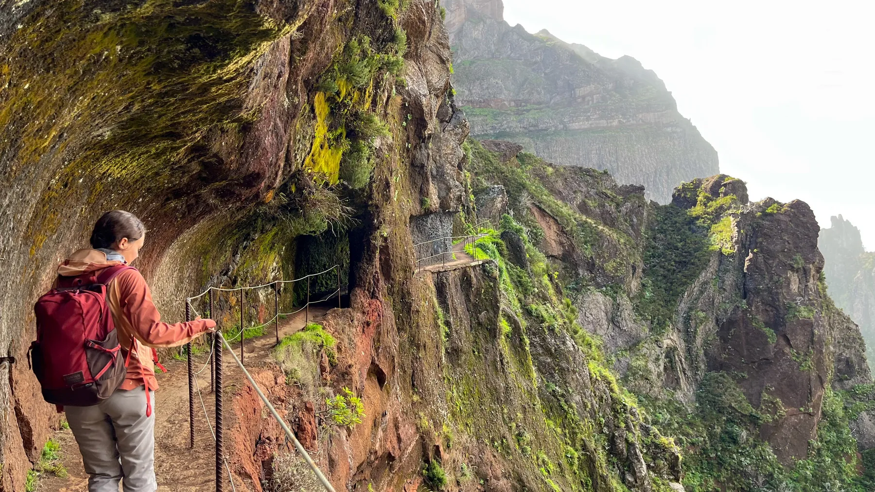 Wanderin auf einem schmalen, grün bewachsenen Bergpfad auf Madeira