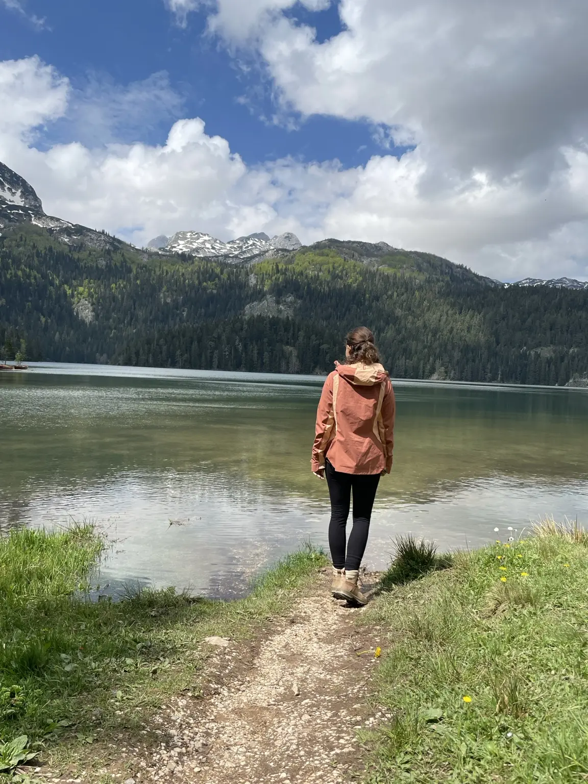 Wanderin am Ufer des Schwarzen Sees vor bewaldeten Bergen mit Schneefeldern