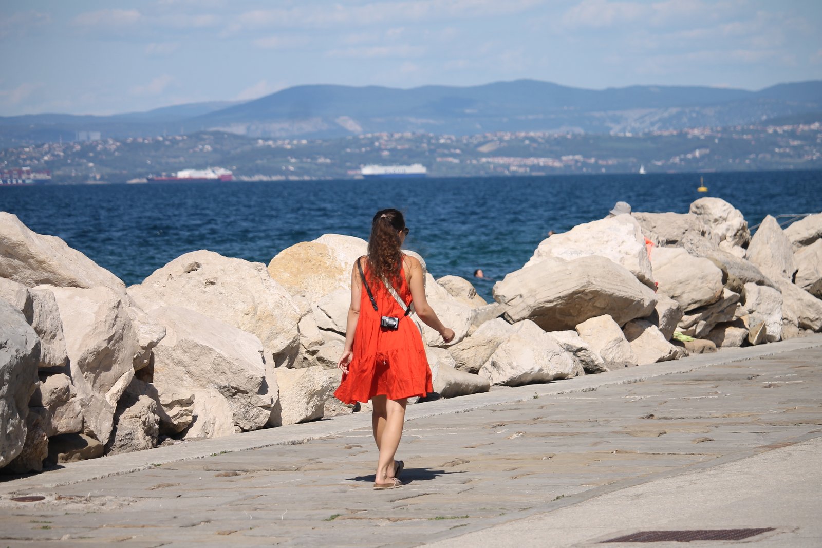 Frau in rotem Kleid auf einer steinernen Promenade an der Adria
