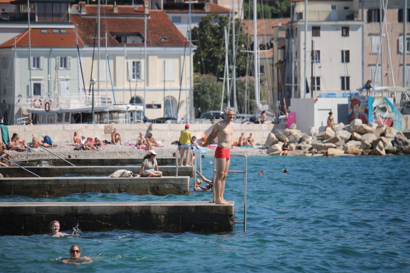 Badende an einer Badestelle mit Hafen und Häusern an der slowenischen Küste