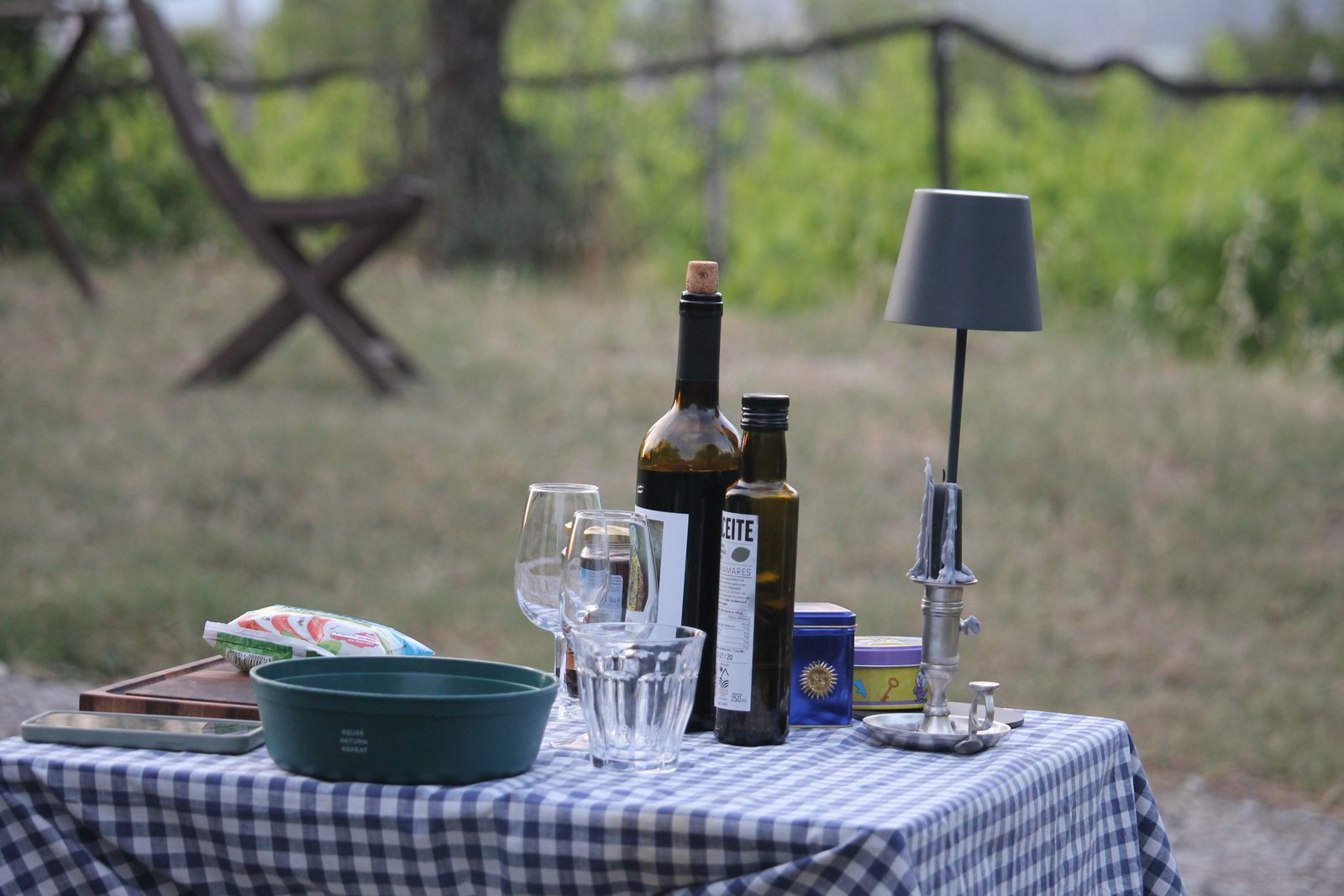 Tisch mit Wein, Olivenöl, Gläsern und Lampe vor einem Weinberg
