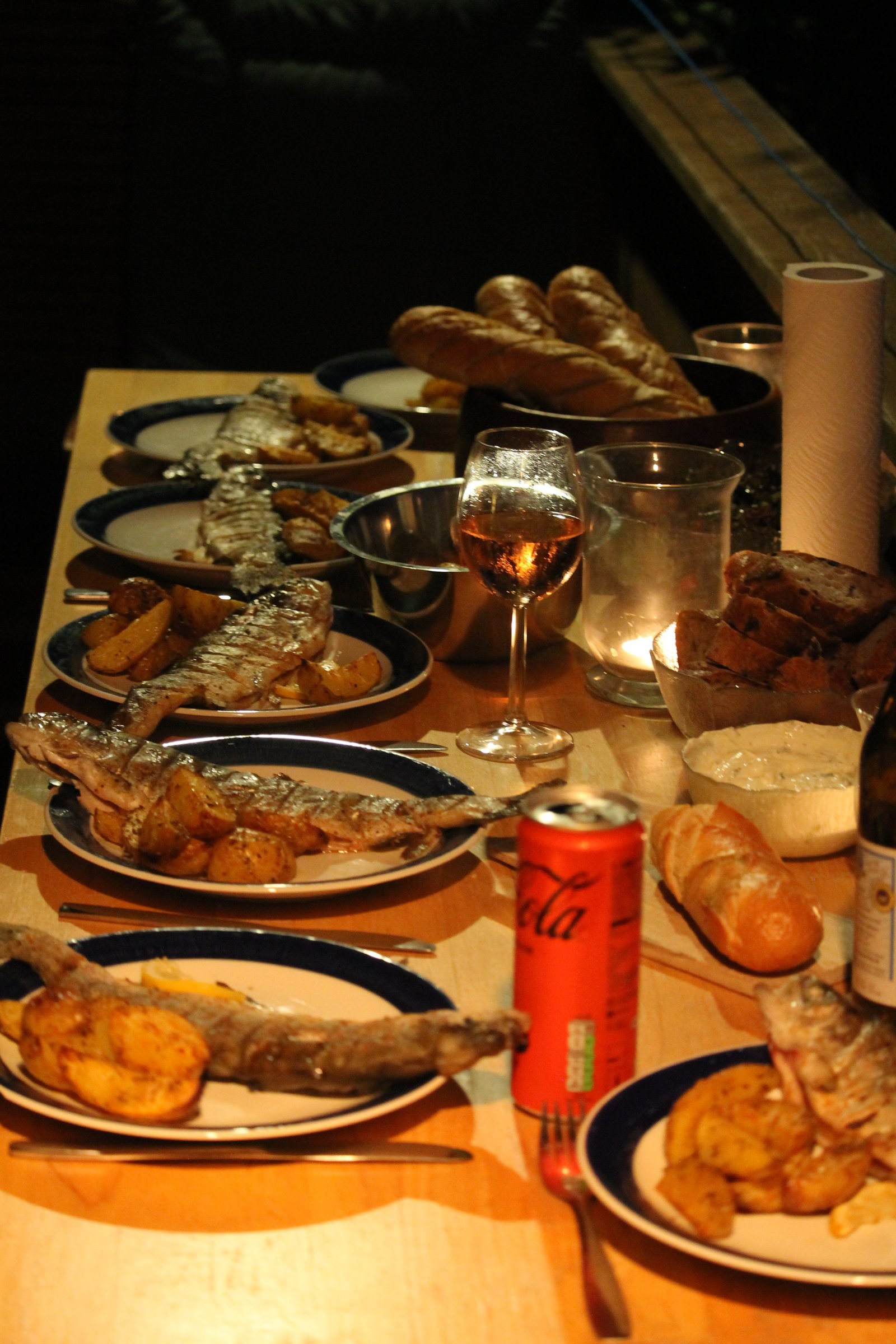 Gegrillter Fisch, Kartoffeln, Brot und Wein auf einem langen Tisch am Attersee