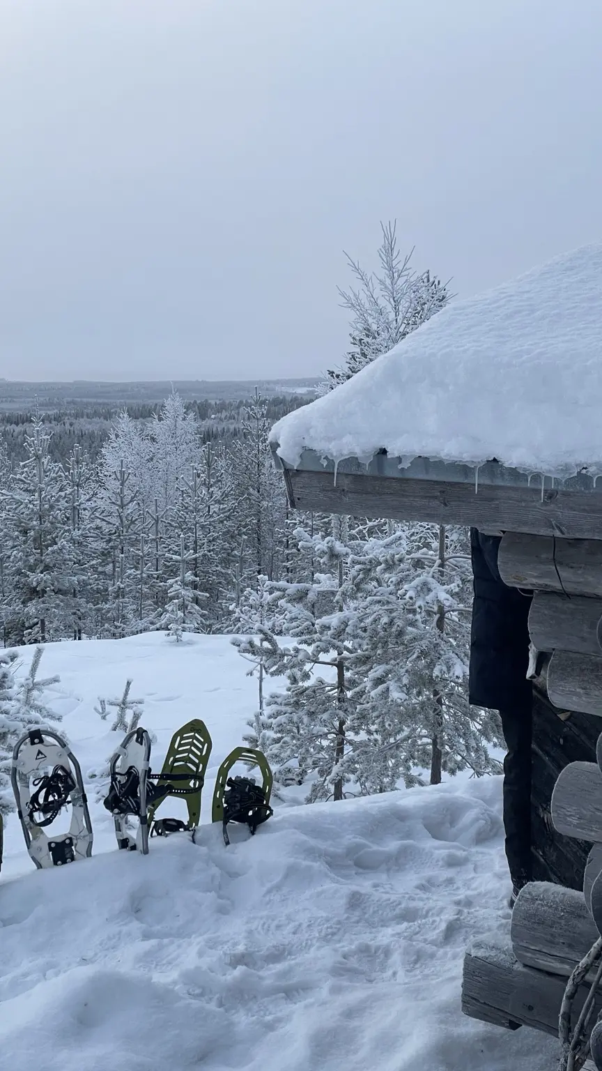 Schneeschuhe stehen vor einer tief verschneiten Blockhütte in Finnisch-Lappland